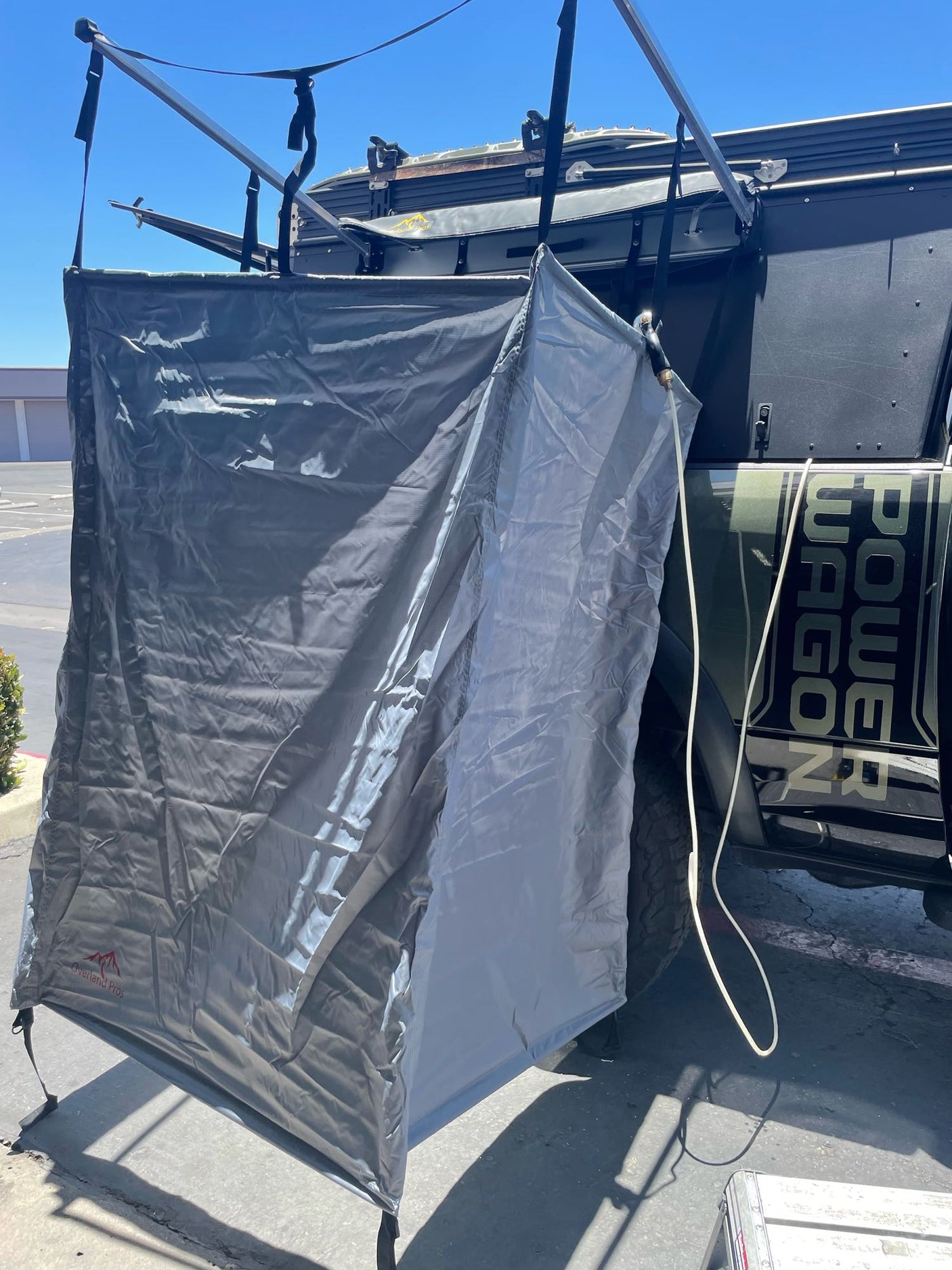An Overland Pros privacy shower tent attached to a Power Wagon via roof rack, with a hose visible, perfect for RV rental adventures.