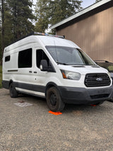 White Ford Transit rv rental campervan, parked on a gravel lot with orange leveling blocks under its tires.
