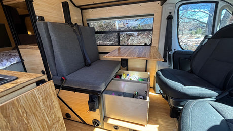 RV rental interior: Custom wood-paneled camper with a comfy bench seat, table, and practical storage drawers.