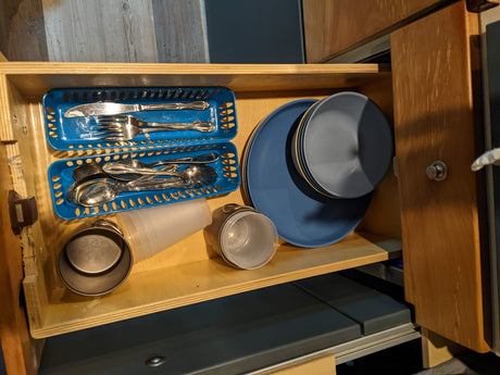An organized RV rental kitchenette, featuring neatly arranged blue plates, bowls, and silverware, ideal for travel and camping meals.