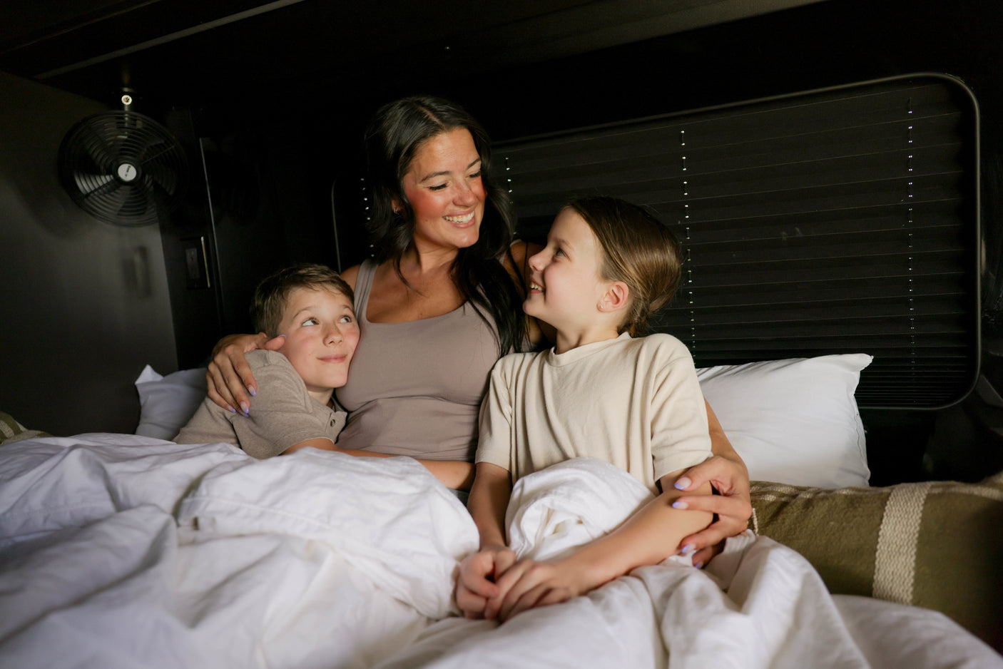 Cozy family time in an RV rental bed! A mother and her children snuggle, sharing smiles during their travel adventure.