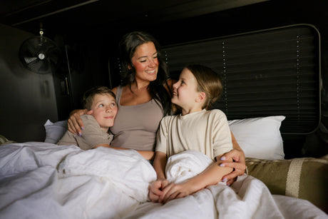 Cozy family time in an RV rental bed! A mother and her children snuggle, sharing smiles during their travel adventure.