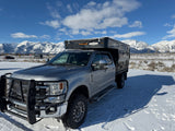 Silver Ford Super Duty truck featuring a Four Wheel Camper, parked in a snowy mountain scene. Great rv rental option!