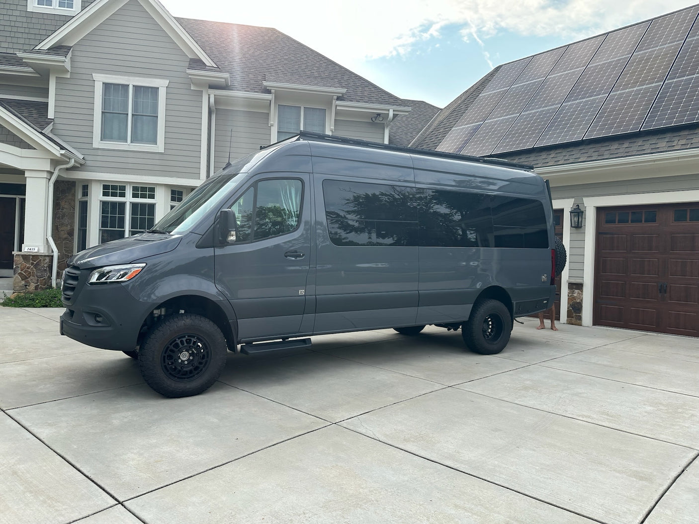 Gray custom camper van, suitable for rv rental, parked on a driveway with a house and solar panels in the background.