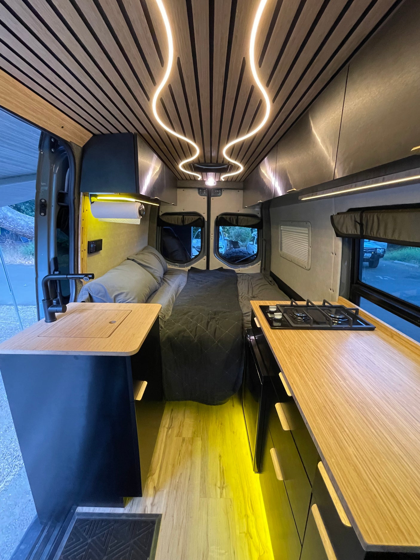 Explore this high-end RV rental's interior! Features a modern wood ceiling with curved LEDs, a full kitchen, and comfortable bed.