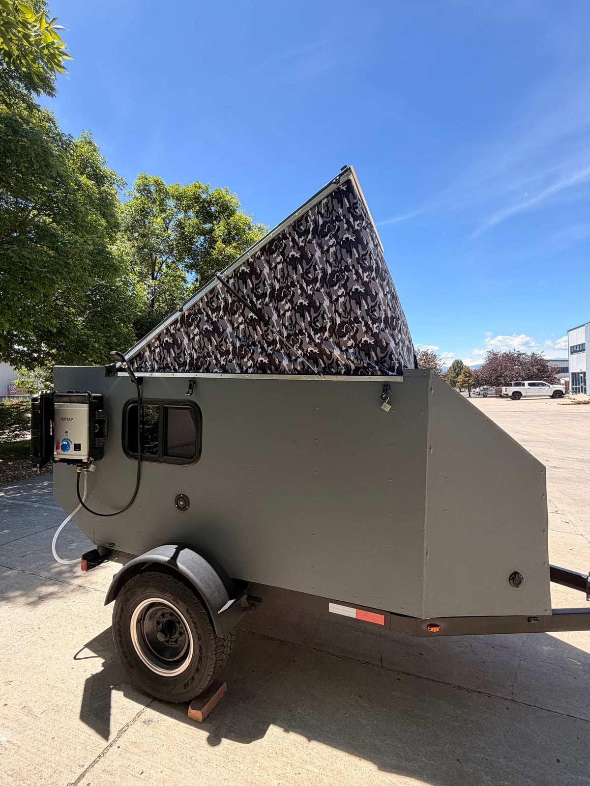 A gray pop-up camper trailer with a camouflage pop-top and outdoor HOTTAP shower, ideal for your next rv rental adventure. — photo 4