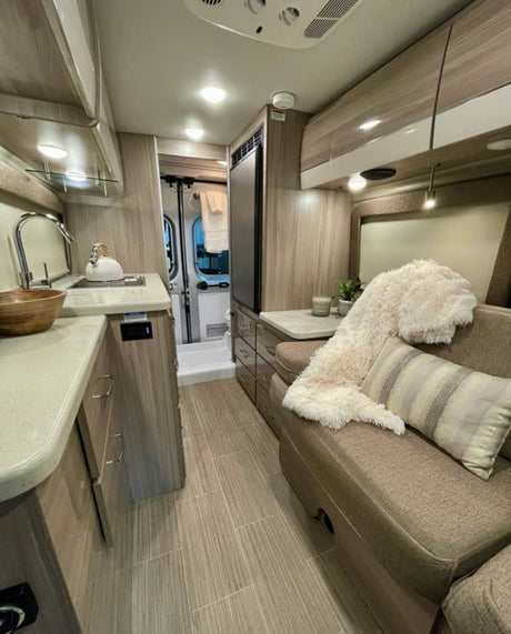 Explore this sleek RV rental: compact kitchen, comfy dinette with a plush throw, and modern amenities for your trip.