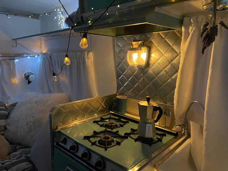 Charming RV rental interior: teal kitchen, retro stove, Moka pot, and string lights create a cozy, home-like feel. — photo 8