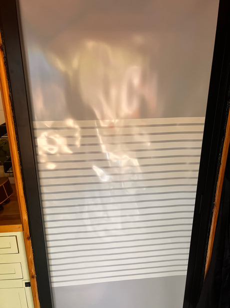 RV rental interior: A window features a two-tone blind; sheer top, striped bottom. Sunlight reflects warmly.