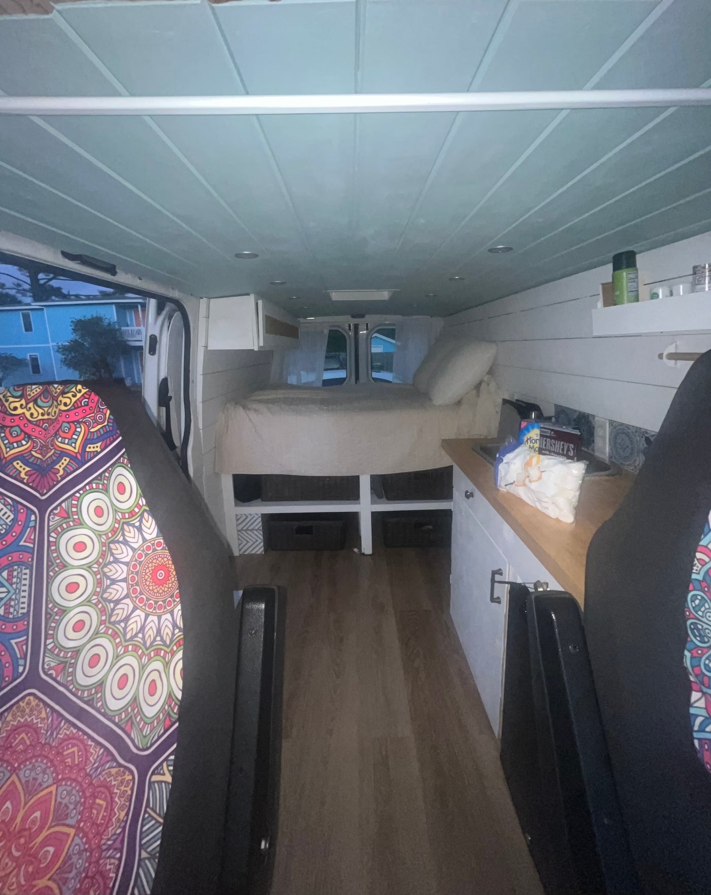 Inside a custom RV rental: light blue ceiling, wood floor, rear bed, and side kitchen with colorful seat details. — photo 9