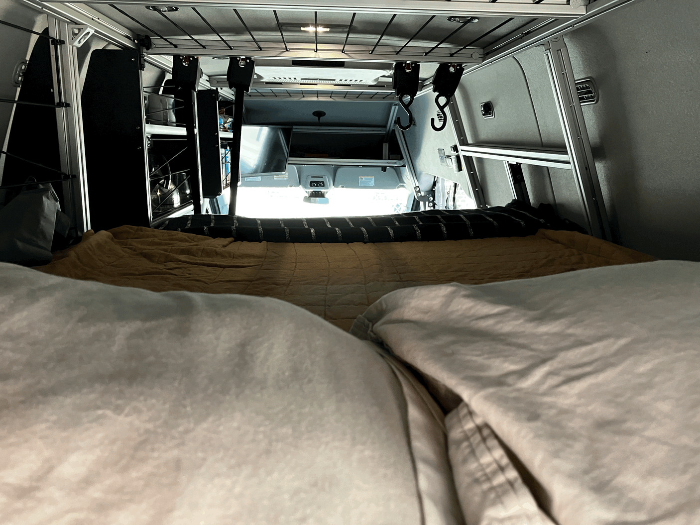 Comfortable bed inside an RV rental, facing the vehicle's cabin with overhead storage and lighting.