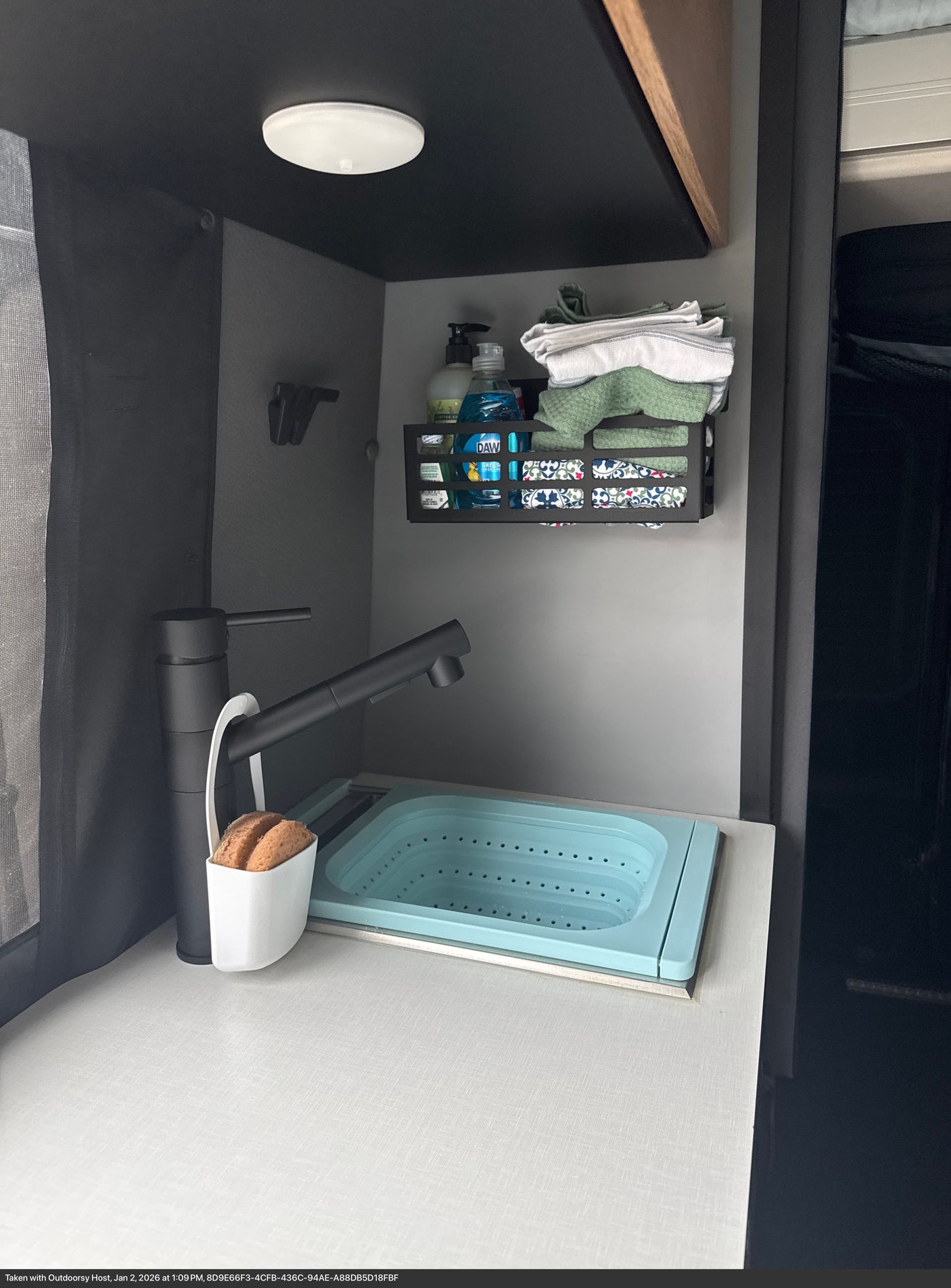 This efficient RV rental kitchen features a black faucet, blue collapsible sink, and wall caddy holding dish soap and towels.