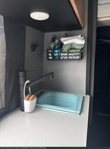 This efficient RV rental kitchen features a black faucet, blue collapsible sink, and wall caddy holding dish soap and towels.