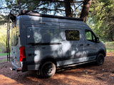 This gray Winnebago Revel 4x4 camper van, perfect for RV rental adventures, is parked in a sun-dappled forest.