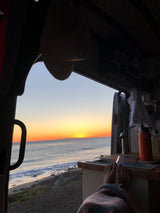 RV rental adventure: Feet up, watching a vibrant ocean sunset from inside the cozy van.