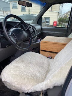 RV rental van interior: steering wheel, custom wood storage, and a cozy white sleeping area. Ideal for a camper conversion.