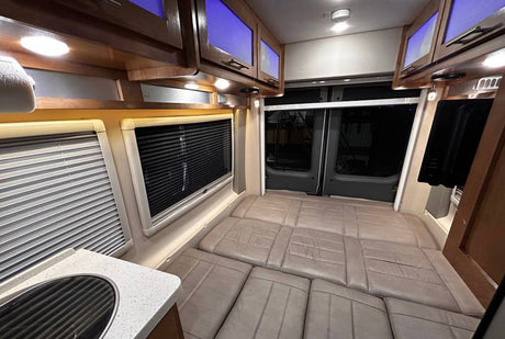 Inside an RV rental camper van, featuring a multi-segment bed, kitchen counter, and overhead cabinets with blue lights.