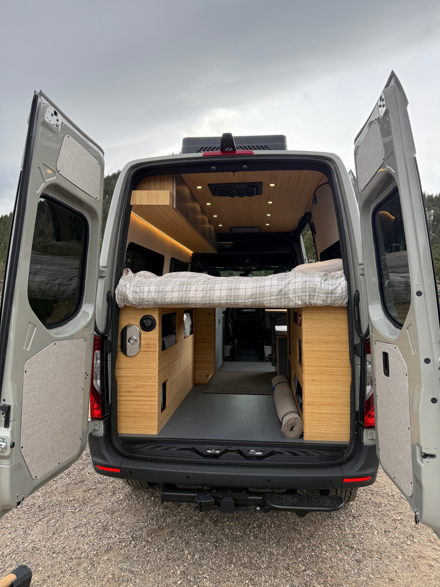 RV rental: Step inside this modern camper van's rear, revealing a cozy bed, wooden interior, and smart storage for travel.
