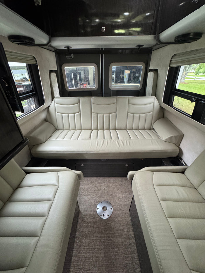 Spacious RV rental interior with cream-colored seating: a long rear sofa and two front chairs, perfect for comfortable road trips.