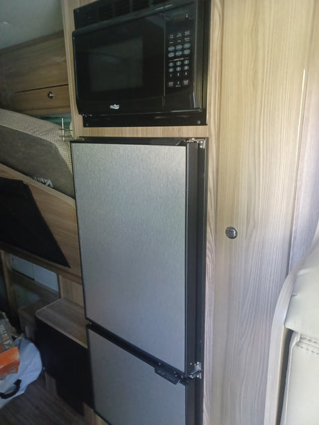 RV rental kitchen featuring a black microwave and two light-grey privacy shades integrated into light wood cabinetry, showcasing a compact interior.