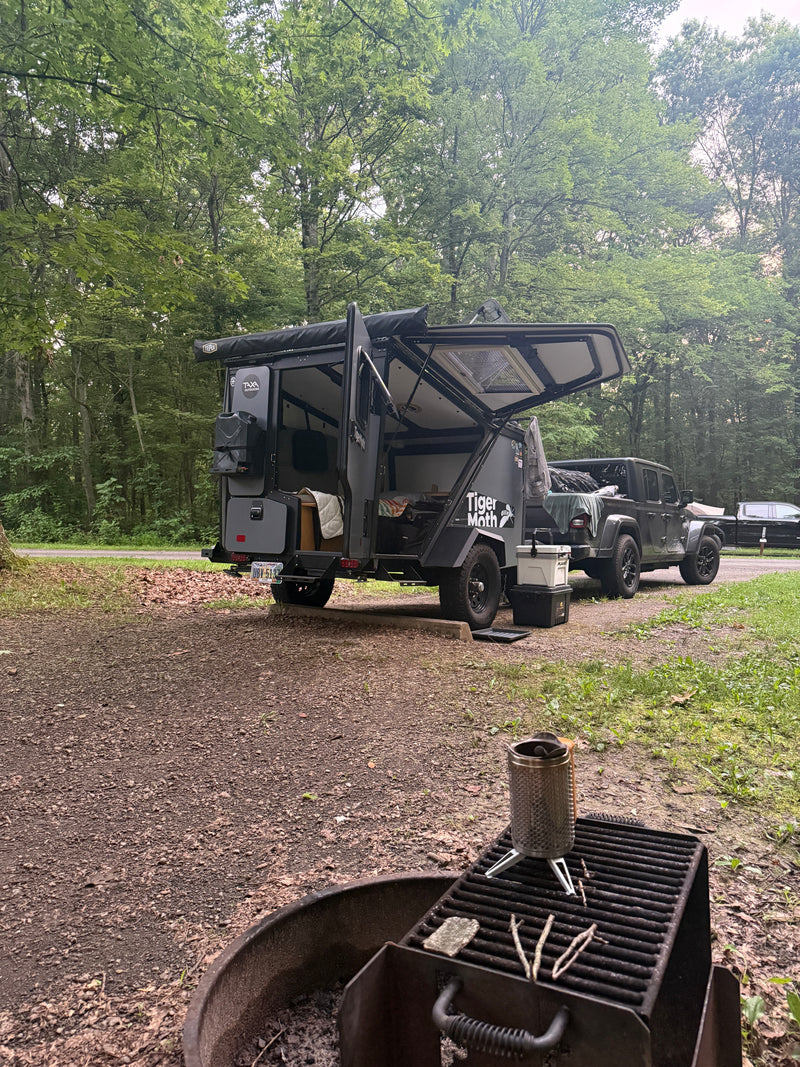 Explore the wild! This rv rental setup features a Tiger Moth overland trailer & Jeep at a forested campsite with a fire pit. — photo 8