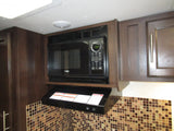 RV rental kitchen showcasing an over-the-range microwave, ventilation hood, and brown-toned tiled backsplash.