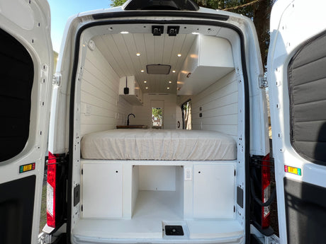 Step inside this white rv rental camper van! Features a cozy bed, sleek mini-kitchen, and smart storage for your adventures.