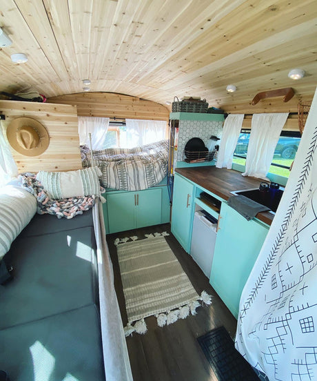 Step inside this stylish RV rental! It features a bright wood and teal interior with a cozy bed and compact kitchen.