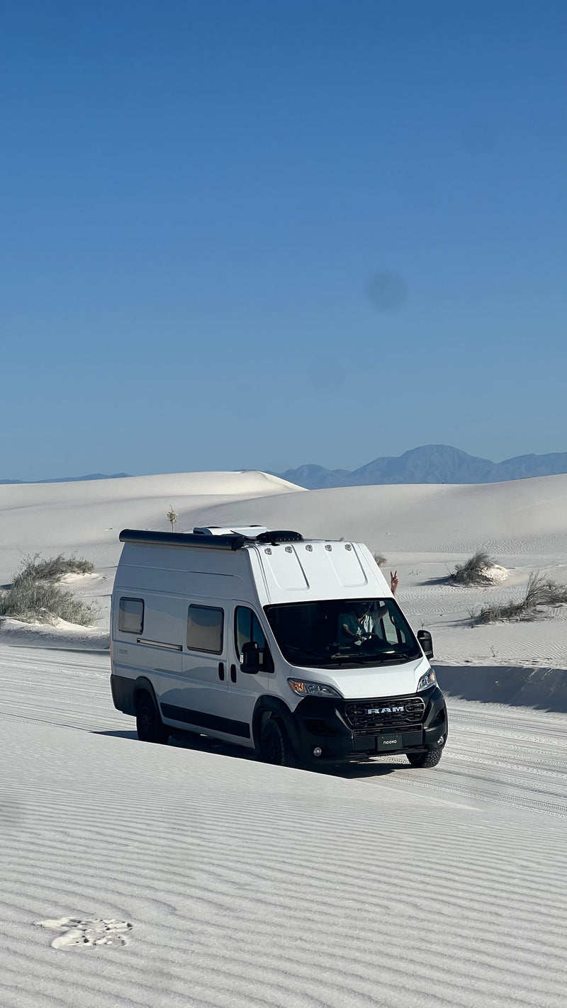 A white camper van from an rv rental drives on pristine White Sands dunes under a clear blue sky. A passenger shows a peace sign. — photo 16