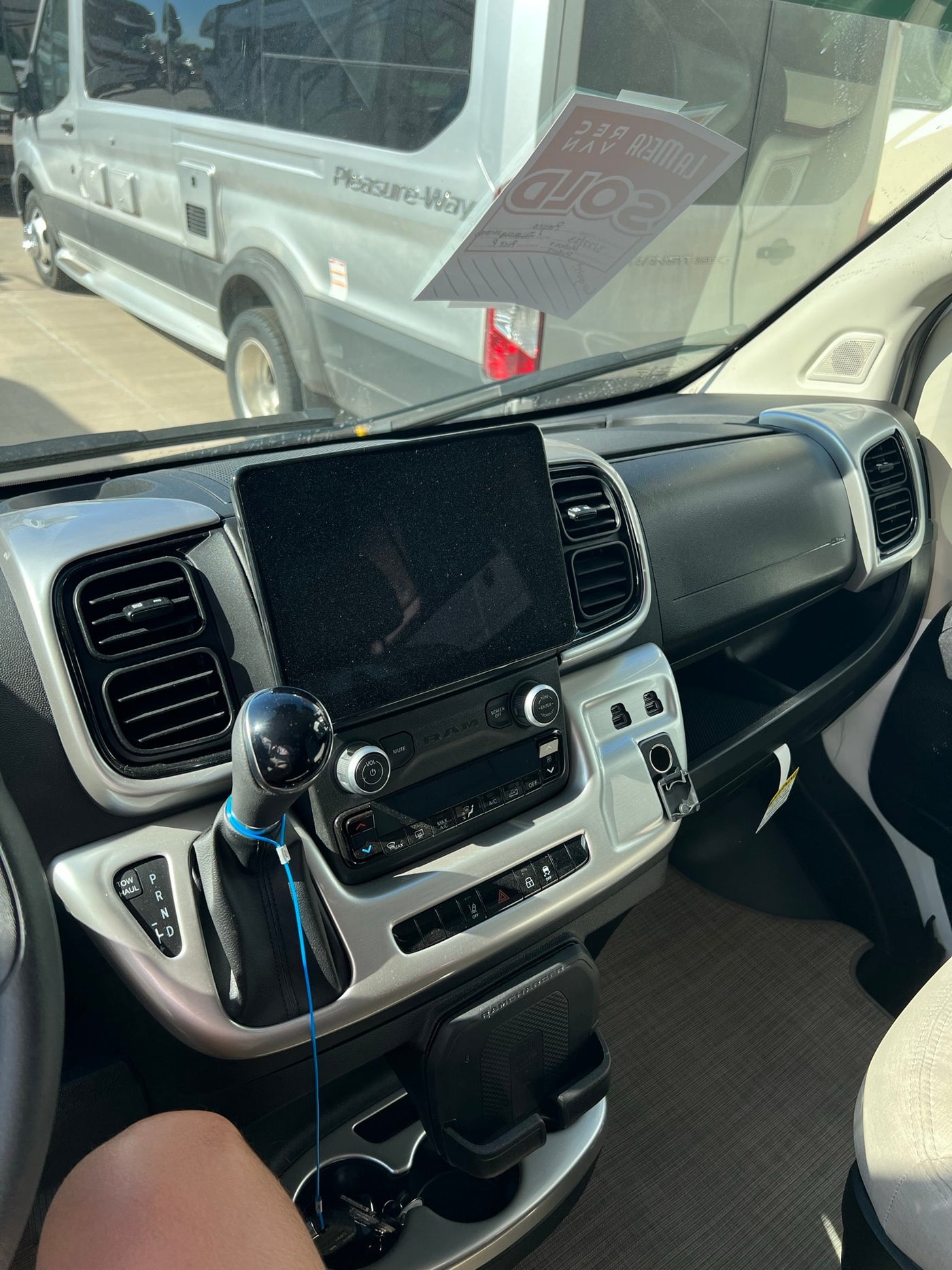  reflections of houses on windows.|This white Tellaro RV rental is parked on a dirt lot by a picnic table and a fence amidst green plants under a cloudy sky.|POV from an RV rental: Ram ProMaster steering wheel with controls — photo 5
