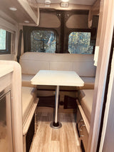 Cozy rv rental interior: A bright dining area with a table, light cushions, and scenic windows, ideal for travel.