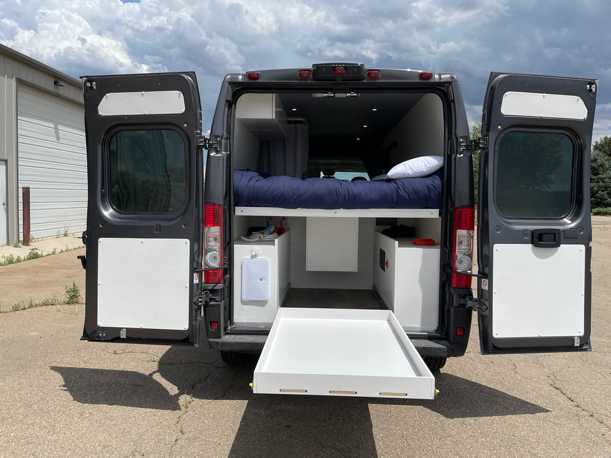 Experience comfort in this RV rental! Rear view of a dark gray camper van with open doors, revealing an elevated bed, interior storage, and pull-out tray.