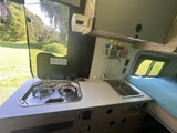 This rv rental features a compact kitchen with a stove and sink, plus a comfy bed and a screen window to the outdoors.