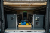 Under-bed storage in an RV rental, showcasing custom cabinets with power outlets and a central pull-out drawer for gear.