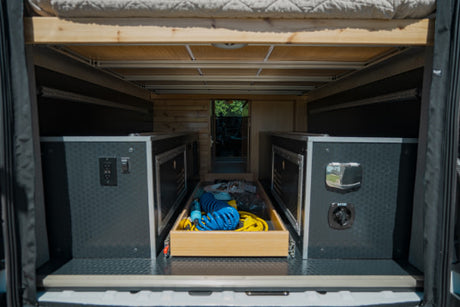 Under-bed storage in an RV rental, showcasing custom cabinets with power outlets and a central pull-out drawer for gear.