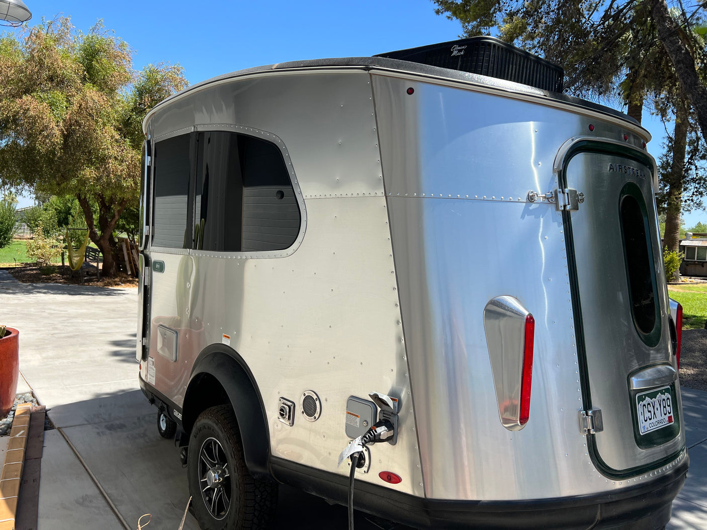 This shiny silver Airstream travel trailer, ideal for an RV rental, is parked and connected, sporting a Colorado plate.