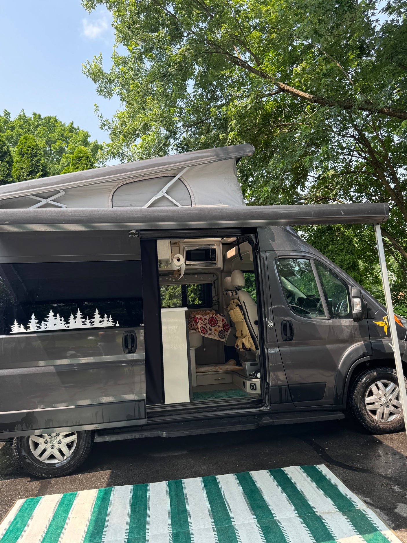 Spacious dark gray RV rental with a pop-top roof and open side door revealing a cozy interior, set up outdoors.