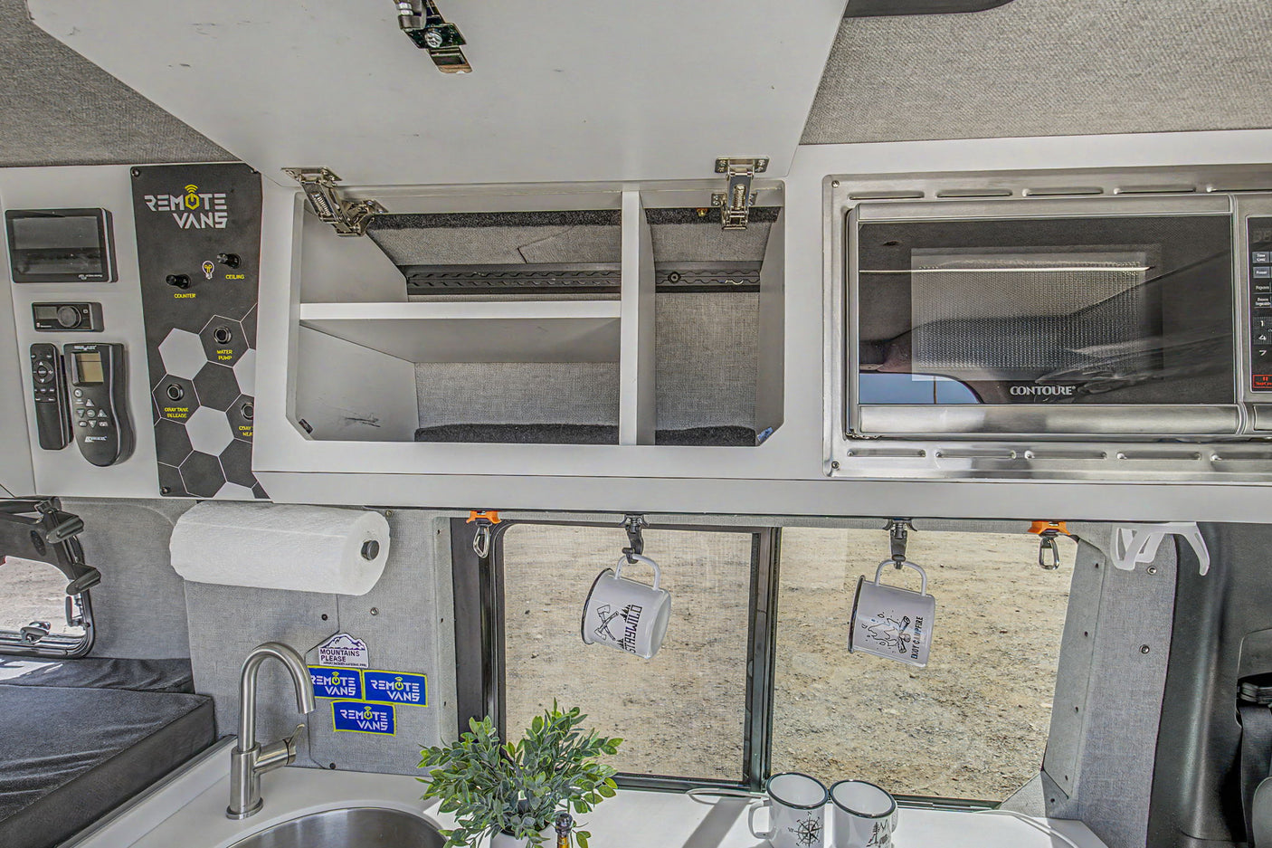 An rv rental's organized interior: kitchen sink, microwave, overhead storage, and a 'Remote Vans' control panel.