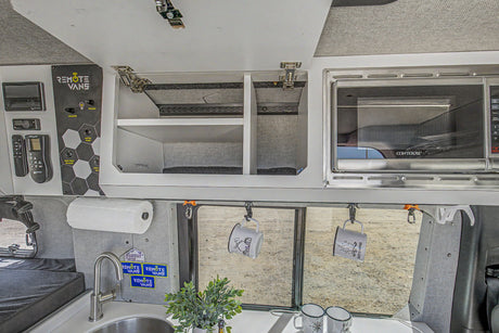 An rv rental's organized interior: kitchen sink, microwave, overhead storage, and a 'Remote Vans' control panel.