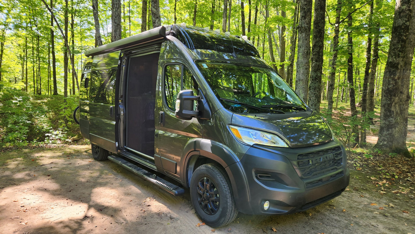 Dark green Airstream camper van, ideal for an RV rental, parked on a dirt path in a sun-dappled forest. — photo 3