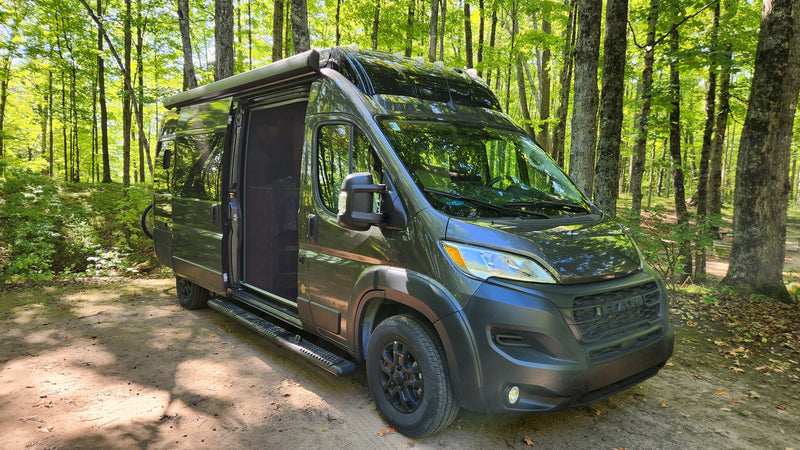 Dark green Airstream camper van, ideal for an RV rental, parked on a dirt path in a sun-dappled forest. — photo 3