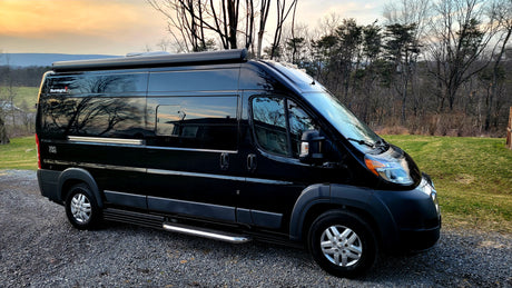 Experience adventure with this sleek black RV rental, a Sunlight Van Two camper van parked on gravel with a scenic backdrop.