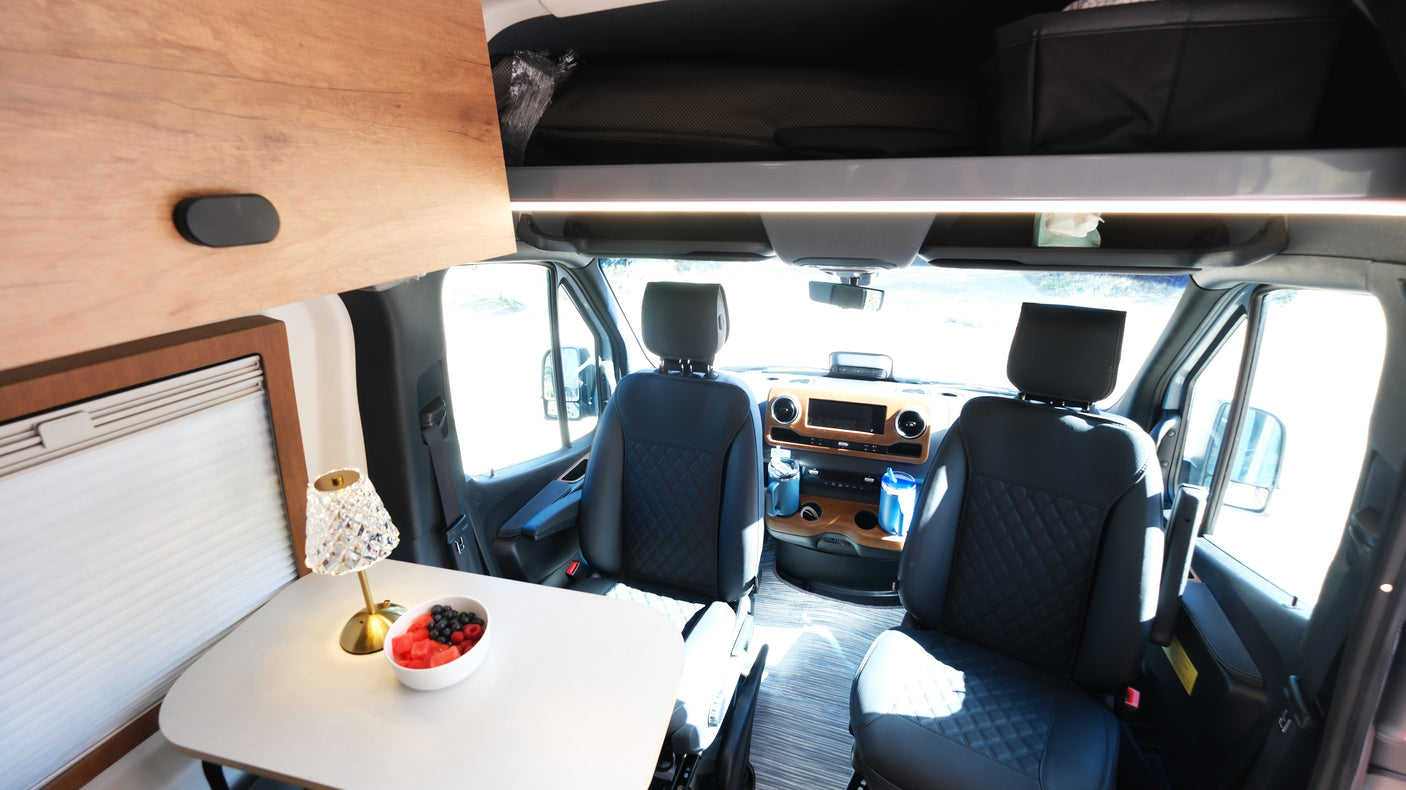 Experience comfort in your RV rental! This modern interior features a dining table with fresh fruit and a well-appointed driving cabin.