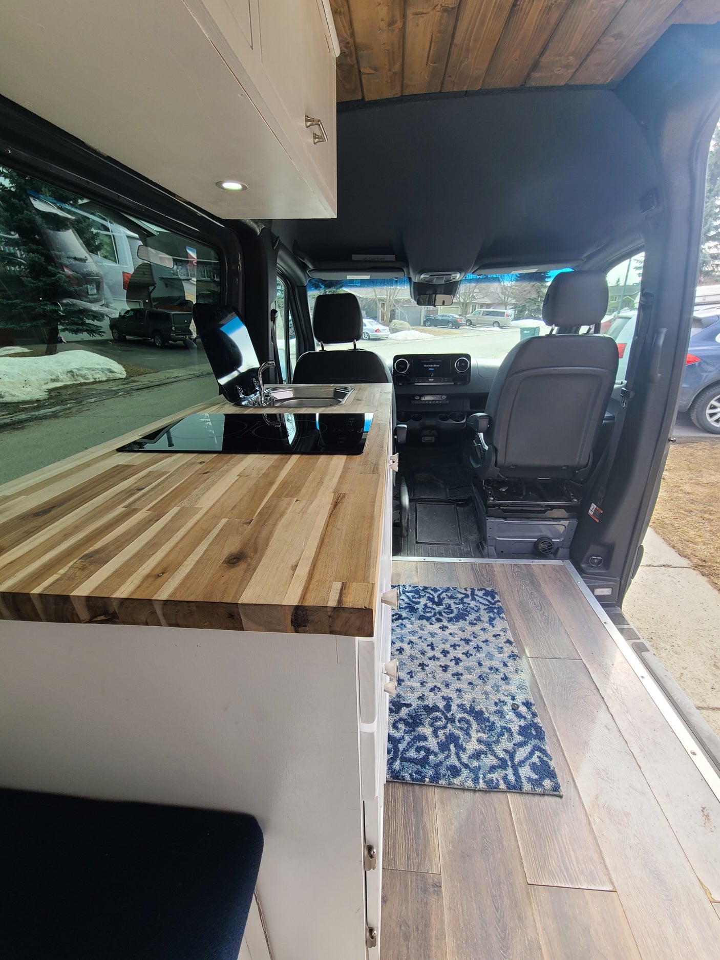 Experience comfort in this RV rental. Custom camper van interior with wood ceiling, kitchenette, cooktop, sink, and wood-look flooring.