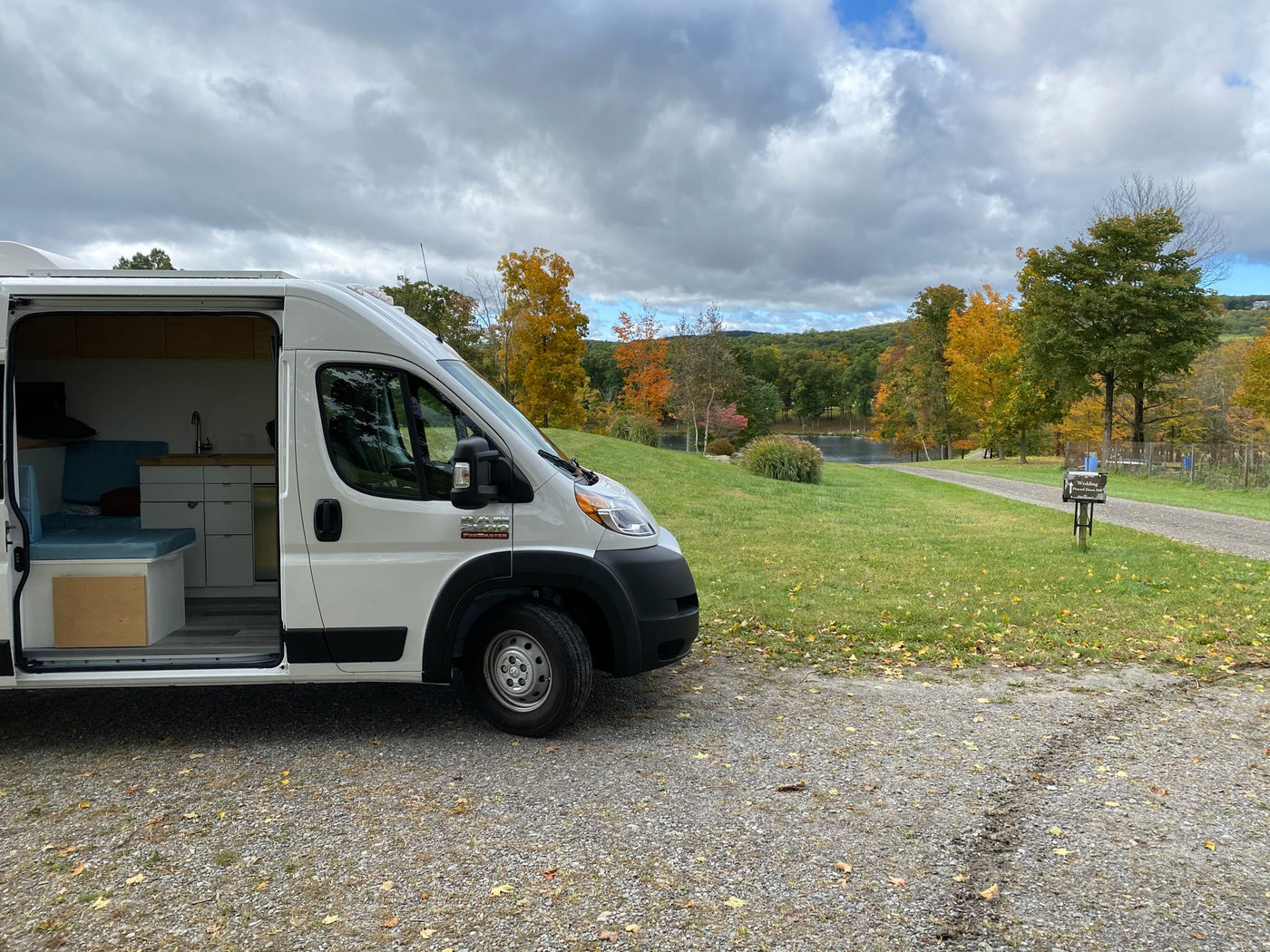  and overhead cabinets for storage in a converted van.|This white Ram ProMaster camper van conversion for rv rental offers a peek inside its cozy interior with a kitchen and seating.|Compact rv rental interior: A hand lifts the seat of a composting toilet integrated under a bed — photo 12