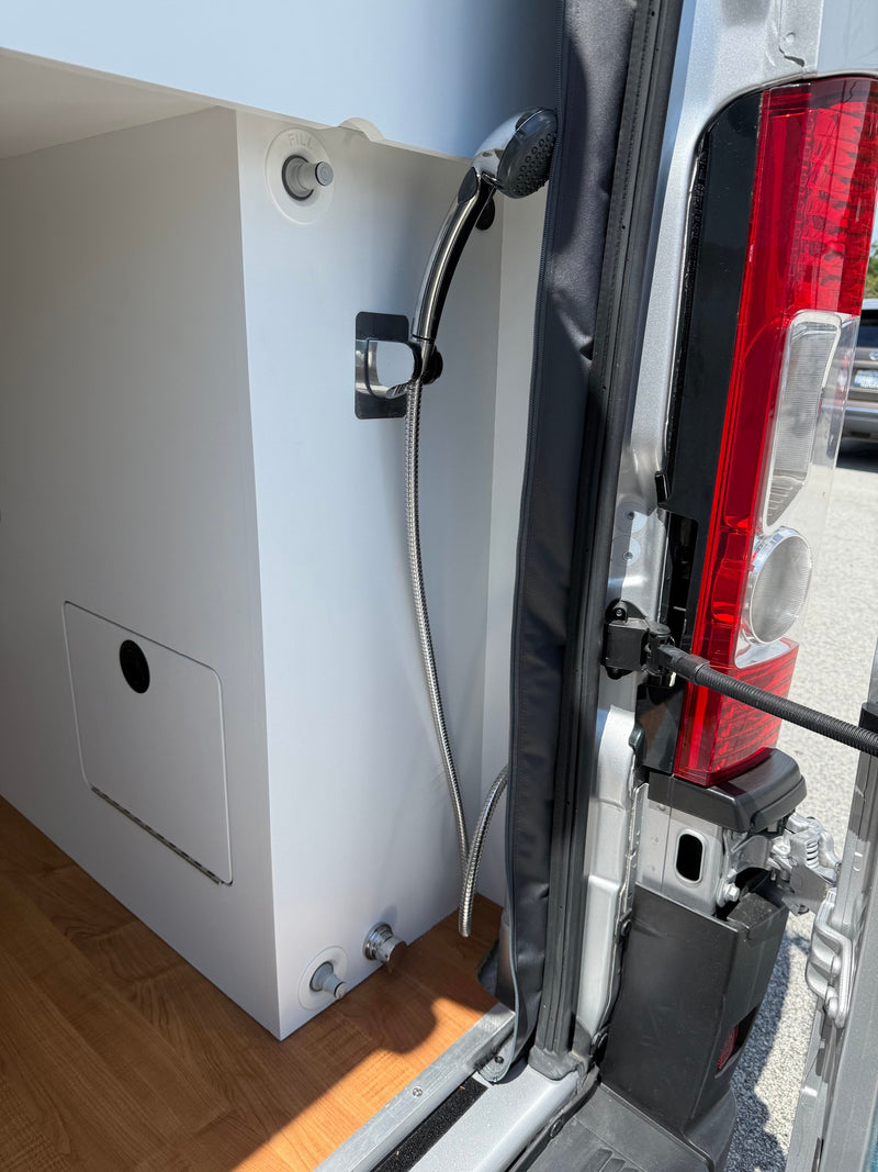  parked under trees.|Compact kitchen in an RV rental featuring a built-in Black+Decker microwave and overhead storage.|RV rental camper van's rear area — photo 3