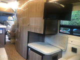 Inside a luxurious RV rental: Modern cabin with sleek cabinetry, a TV, comfy bench seating, and a window view.