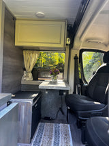 This inviting RV rental interior features a dining nook, scenic window view, cooler, and cozy living space.