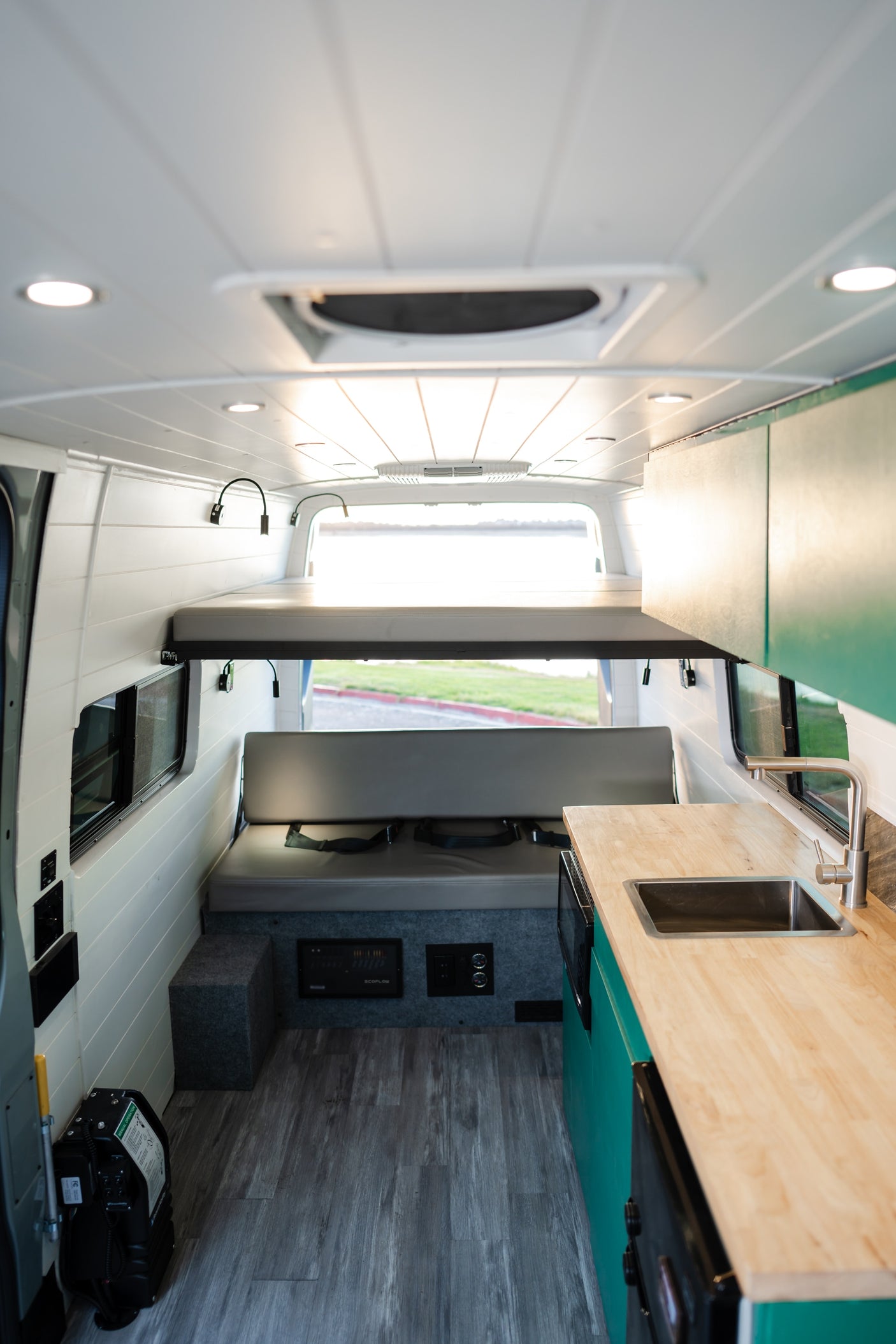 Inside this modern RV rental: bunk bed, kitchen with sink, comfy bench seat, and wood-grain floor.