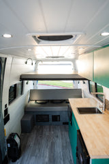 Inside this modern RV rental: bunk bed, kitchen with sink, comfy bench seat, and wood-grain floor.